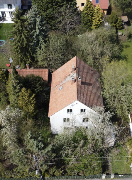 Luftaufnahme eines weißen Hauses mit rotem Ziegeldach, von Bäumen umgeben.