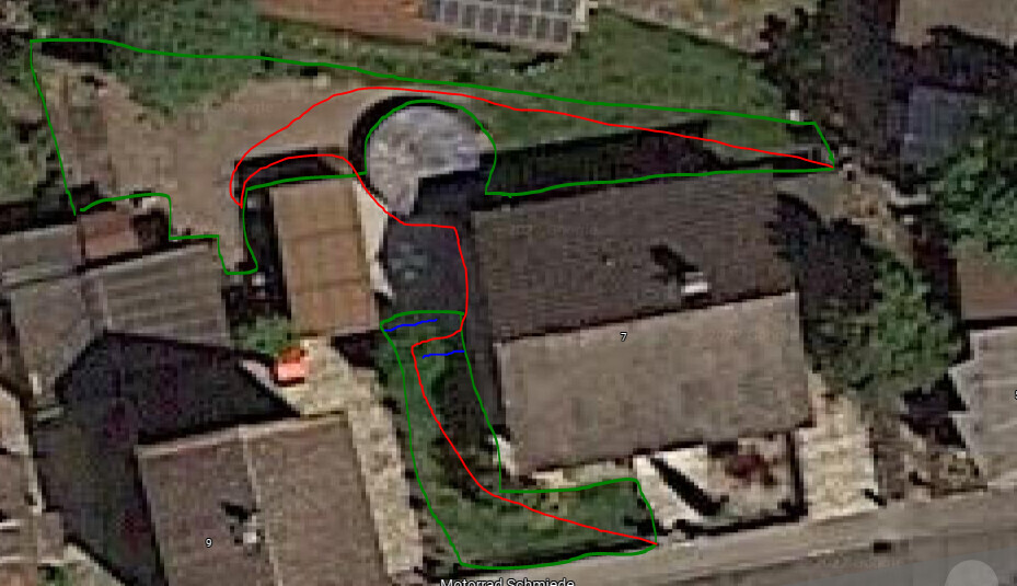 Luftaufnahme eines Gebäudekomplexes mit grünen, roten und blauen Umrissen um Gebäude und Wege.