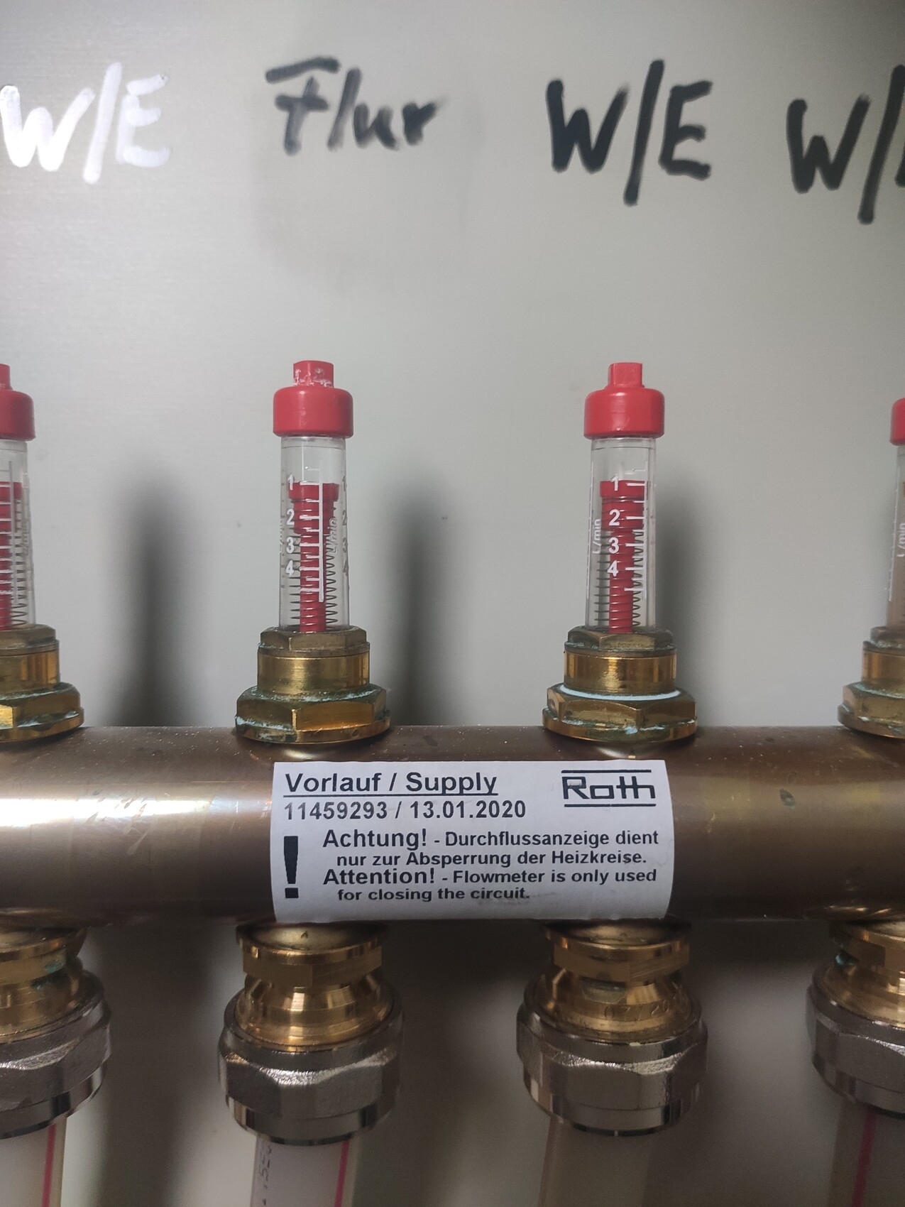 Mehrere Durchflussanzeigen mit roter Flüssigkeit an Kupferrohr, Vorlauf markiert.