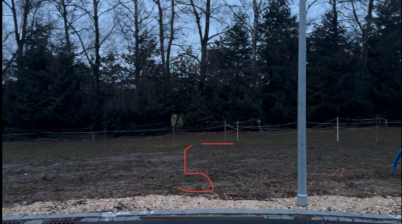 Abenddämmerung: Spielplatz mit Laternenpfosten, Zaun, Bäume; rote 5 auf dem Boden.
