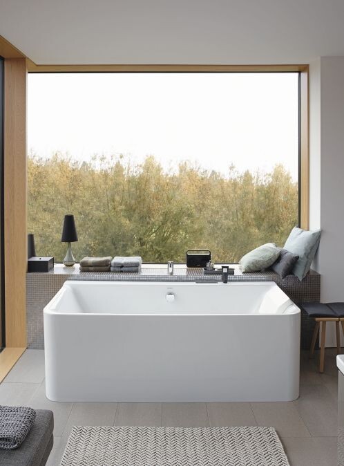 Große freistehende Badewanne vor Fenster mit Blick auf Bäume; Ablage mit Handtüchern.