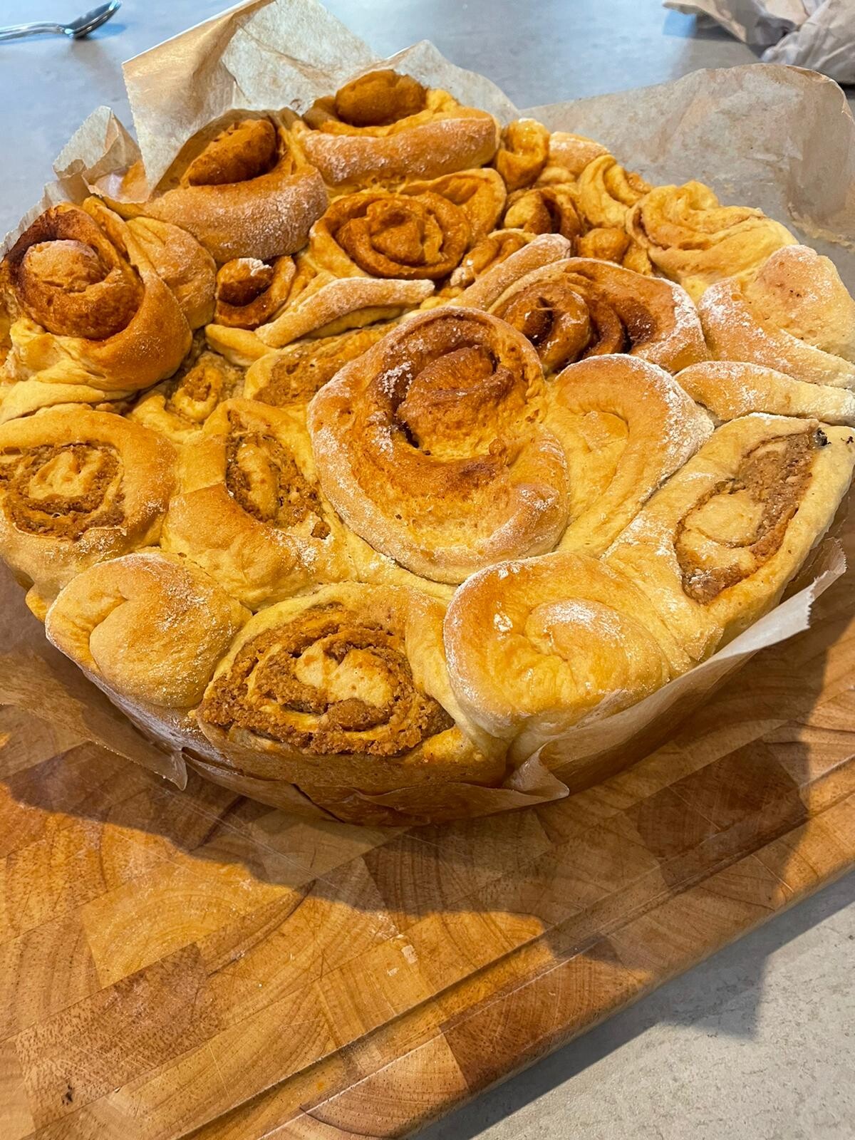 Große Runde Zimtschnecken auf Backpapier, goldbraun, leicht bestäubt.