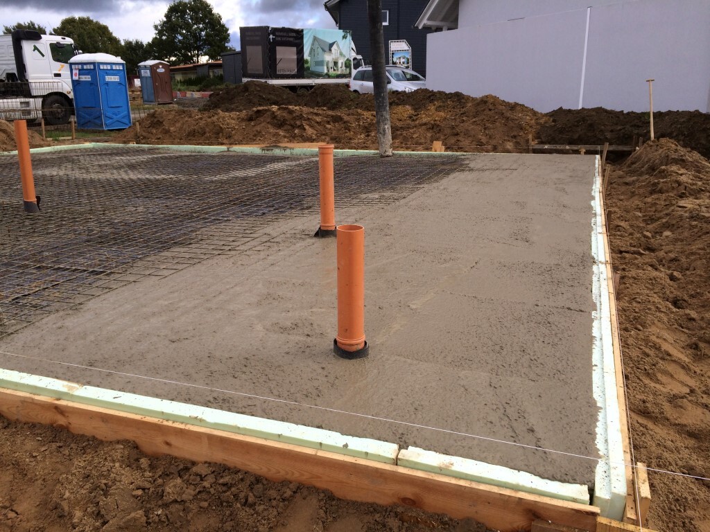 Baustelle: Frischbetonfundament mit Stahlbewehrung, orange Rohrleitungen, Holzformrahmen, Erdarbeiten