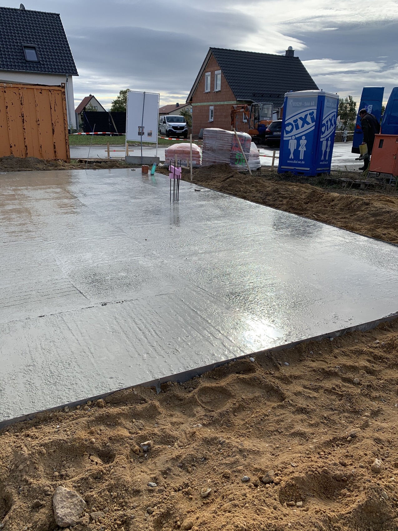 Frisch gegossene Betonplatte auf Baugrube; Baustelle mit Dixis-Container und Bagger.