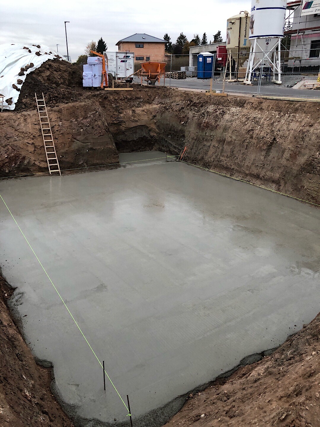 Frisch gegossenes Fundament in Baugrube mit Leiter auf Baustelle