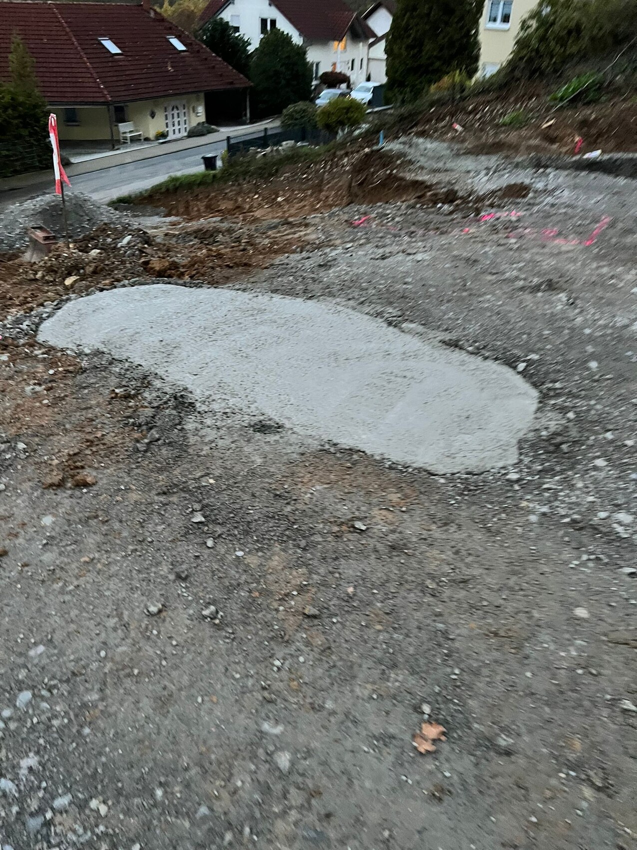 Baustelle mit rundem Betonboden, Erdreich und pinken Markierungen; Häuser im Hintergrund