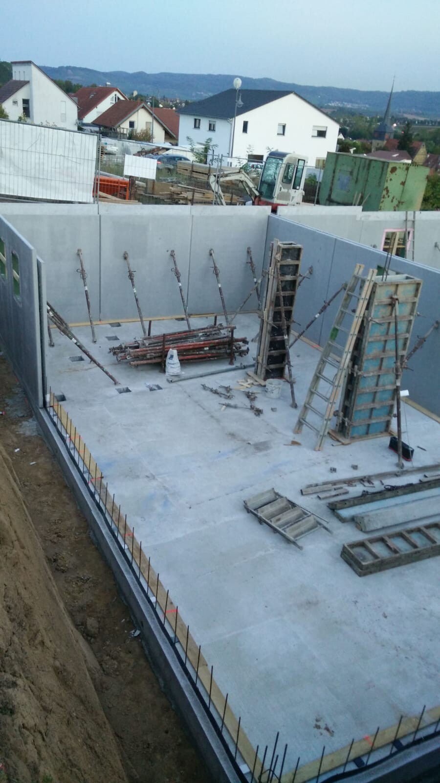 Rohbaustelle: Betonboden, vertikale Stützen, Leitern und Bauwerkzeuge auf einer Baugrube.