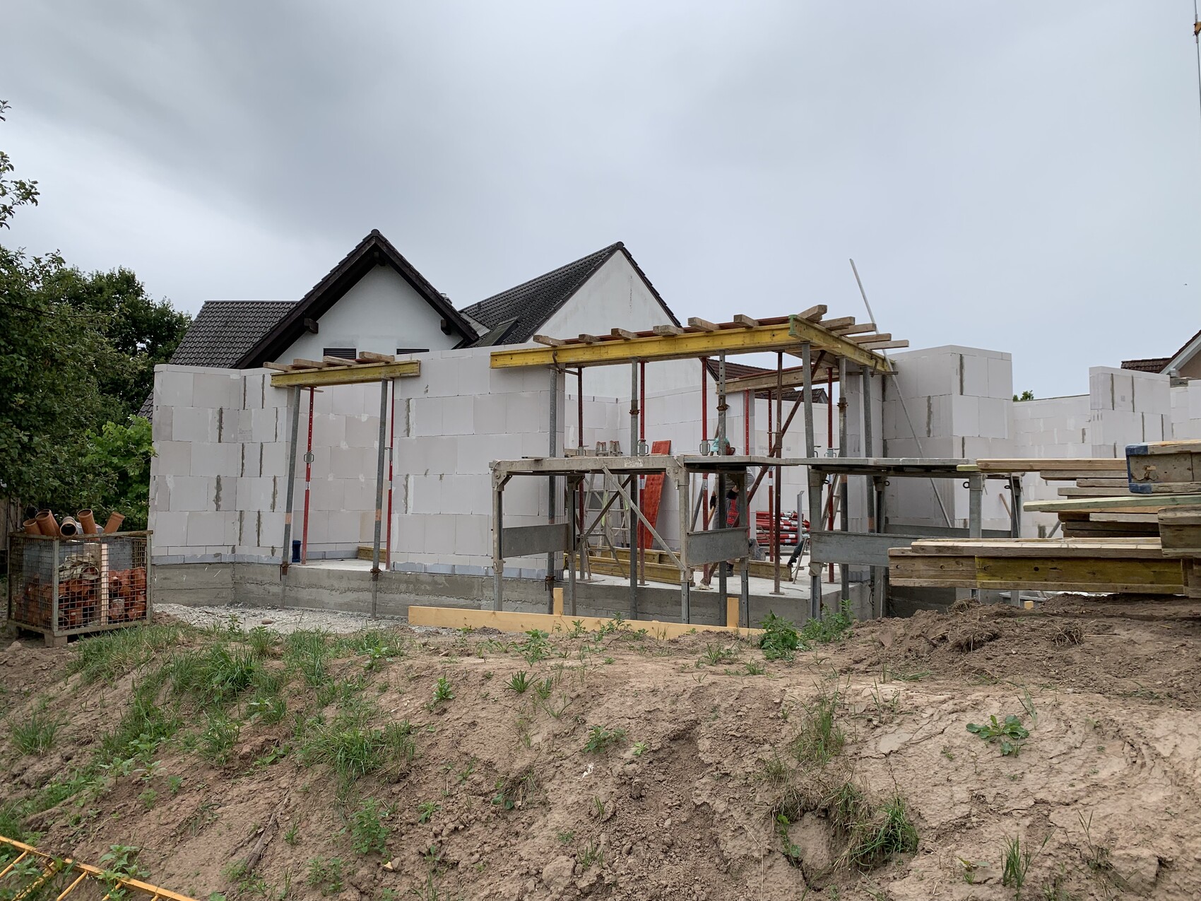 Unfertiges Hausbauprojekt mit weißen Blockwänden, Gerüsten und Baumaterialien.