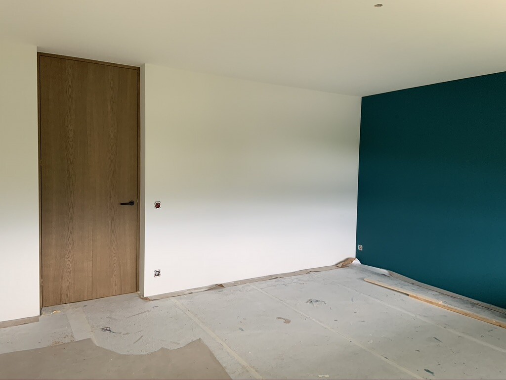 Raum unter Renovierung: Tür links, weiße Wand mittig, tealfarbene Wand rechts, Boden geschützt.
