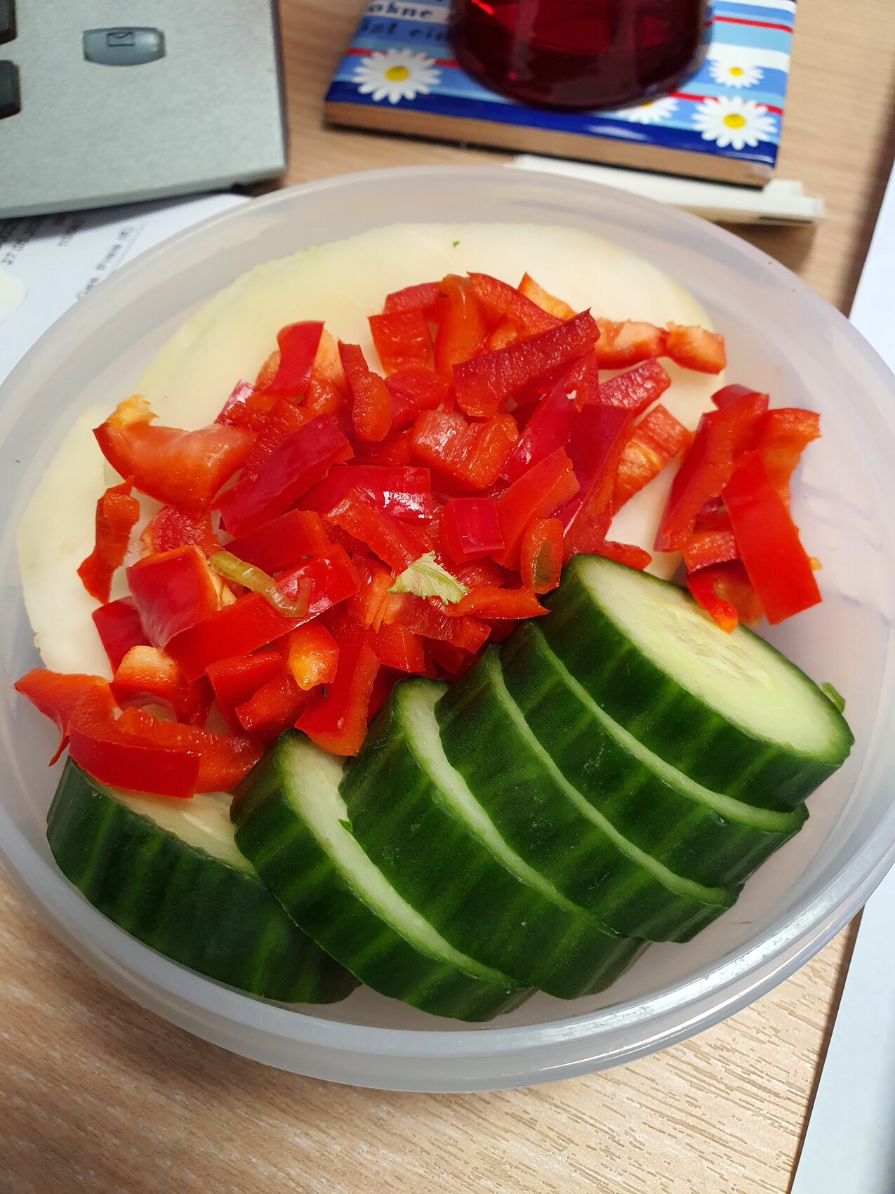 Schüssel mit gehackten roten Paprikastücken und Gurkenscheiben auf hellem Dip.