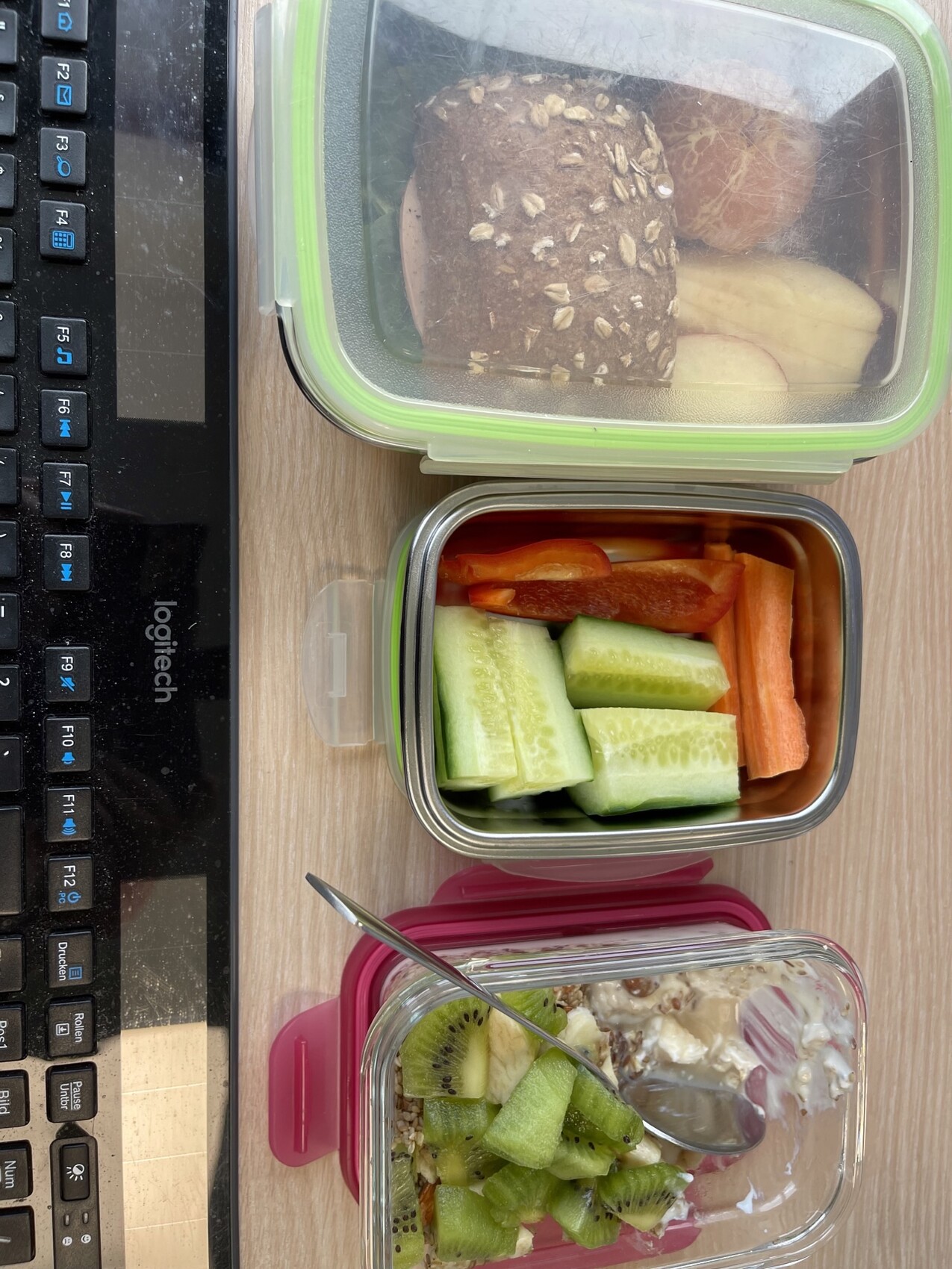 Lunchboxen mit Körnerbrot, Apfel, Gurken- und Karottensticks; Kiwi-Joghurt mit Müsli.