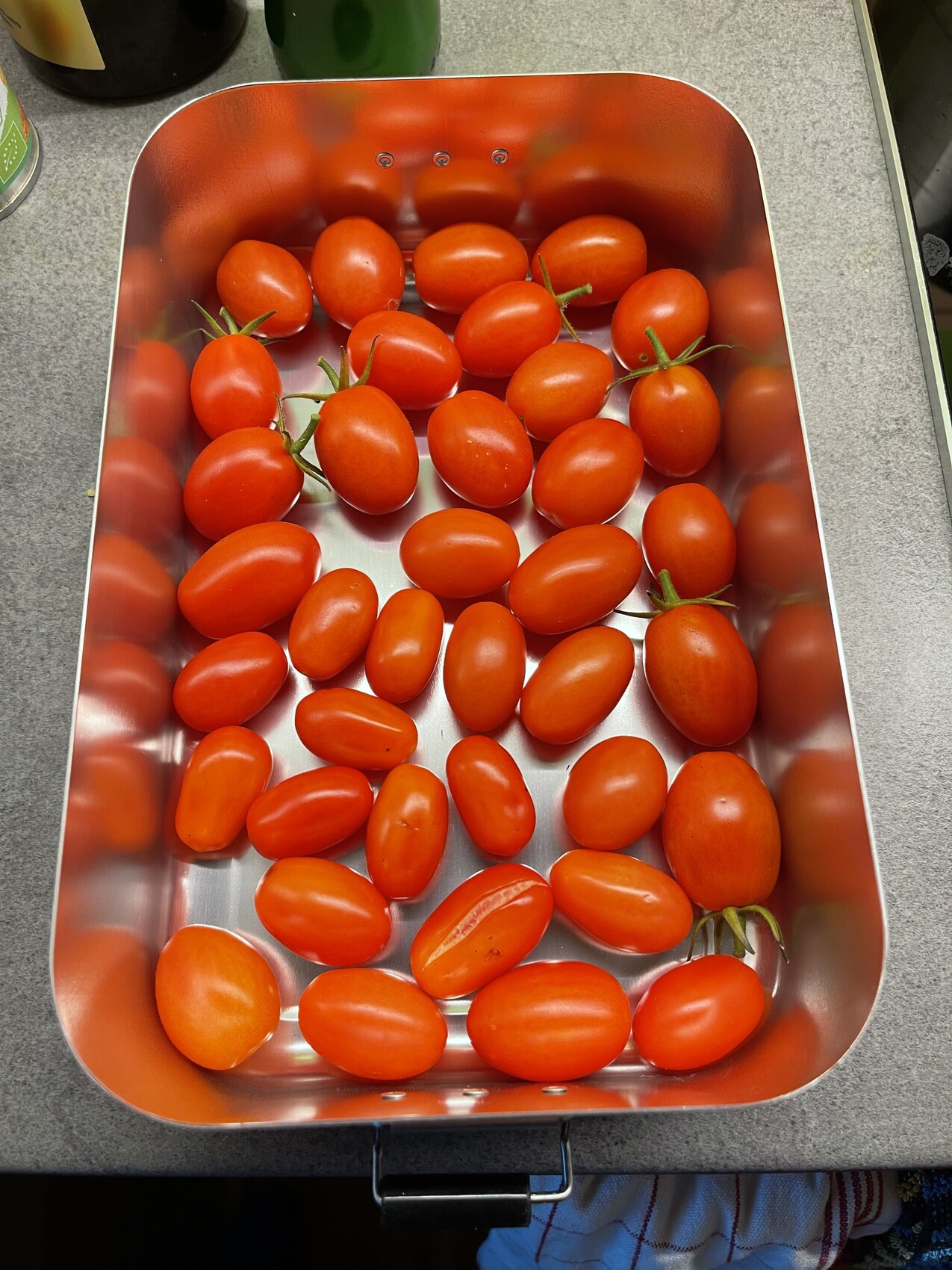 Rote Tomaten in einer Edelstahl-Backform auf einer Küchenarbeitsplatte.