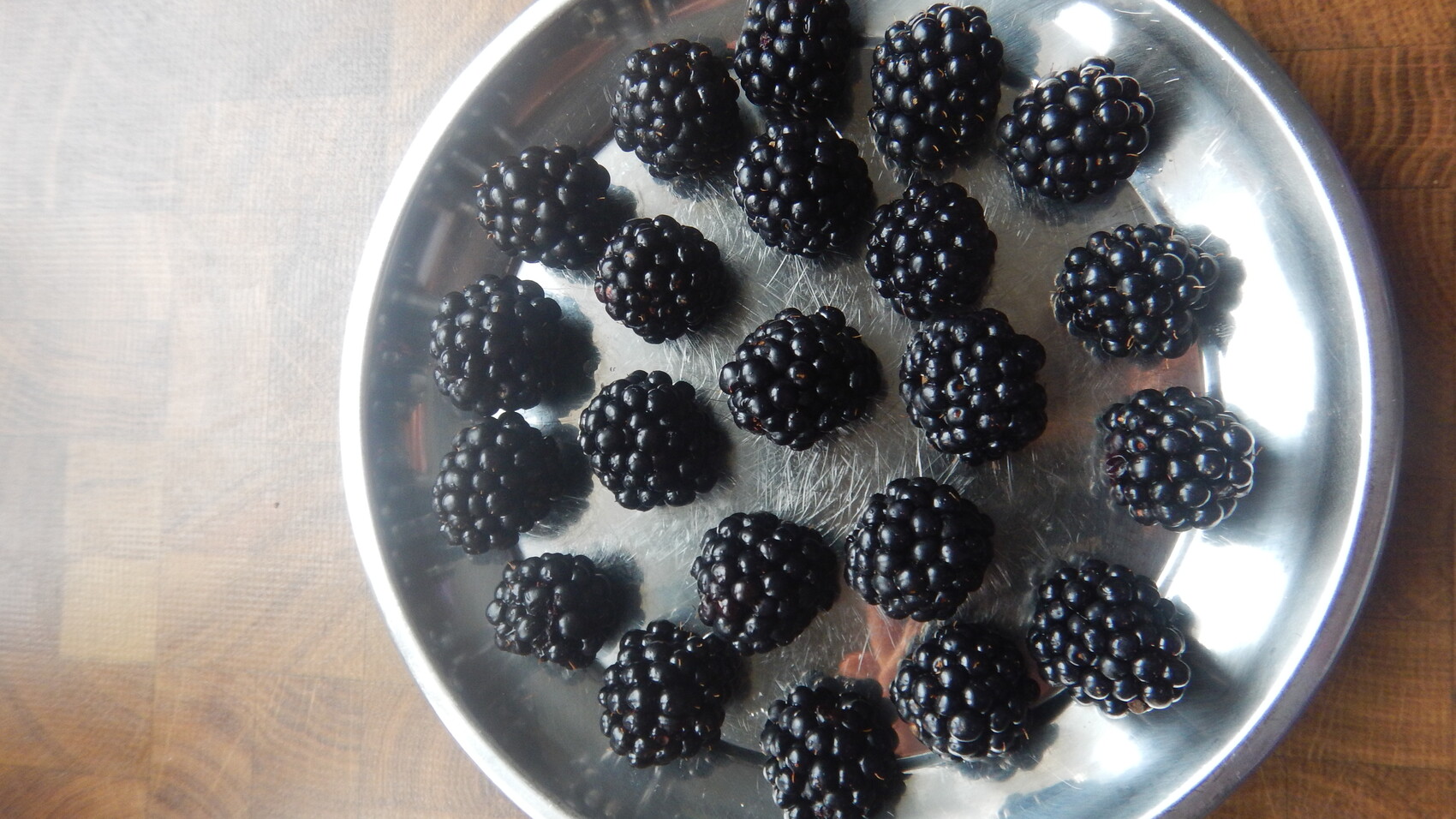 Runde Metallplatte mit mehreren frischen Brombeeren auf Holztisch.