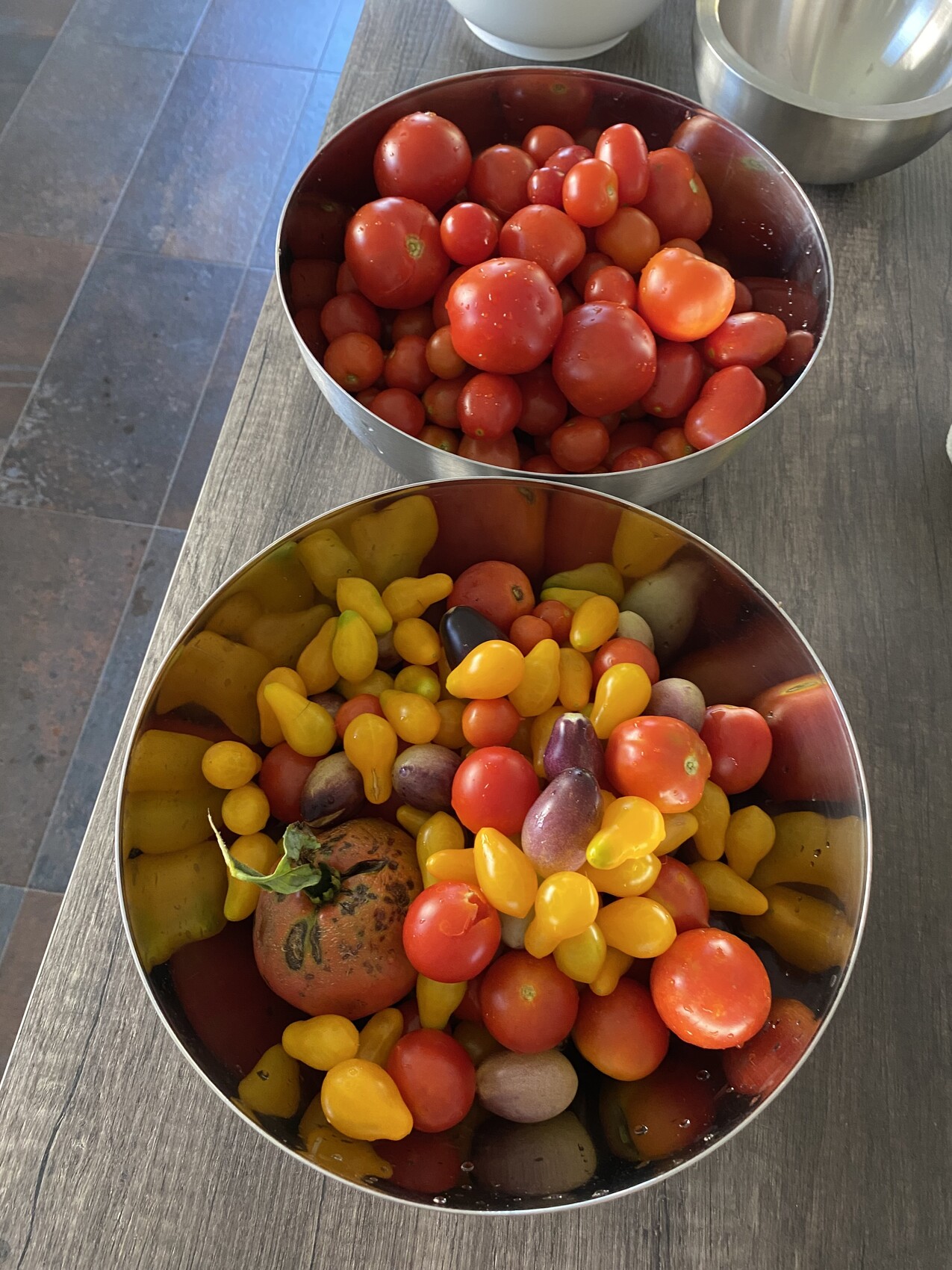 Zwei Edelstahlschalen mit roten Tomaten und buntem Gemüse auf Holztisch.