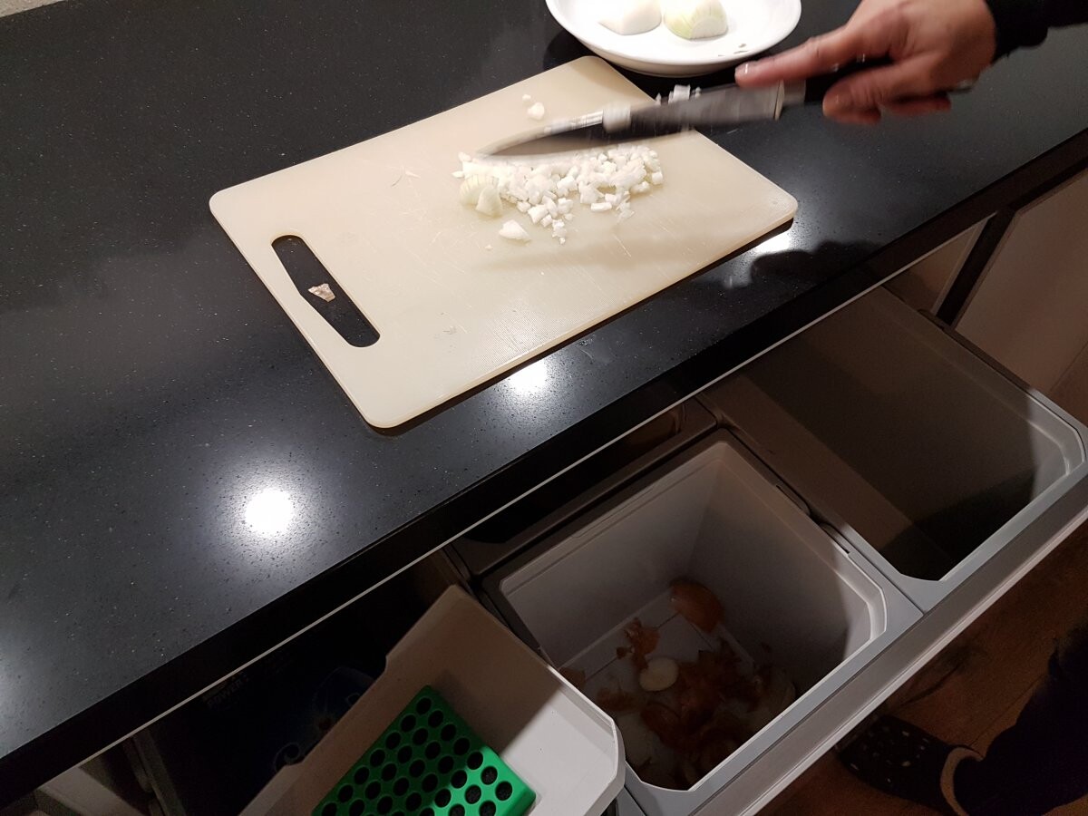Schneidebrett mit gehackten Zwiebeln, Hand mit Messer auf dunkler Küchenarbeitsplatte