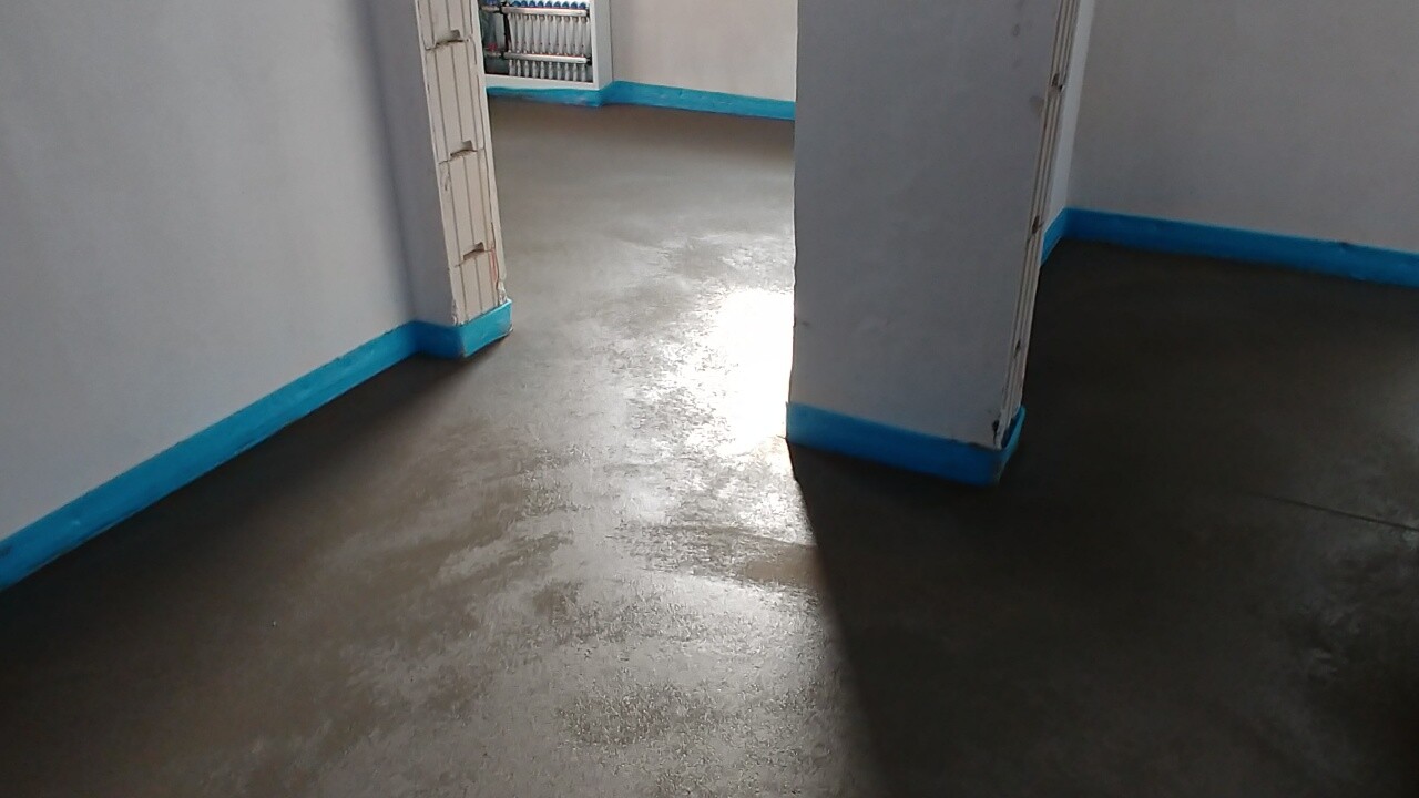 Innenflur mit blauer Fußleiste, feuchtem Boden und Durchgang in einen Raum.