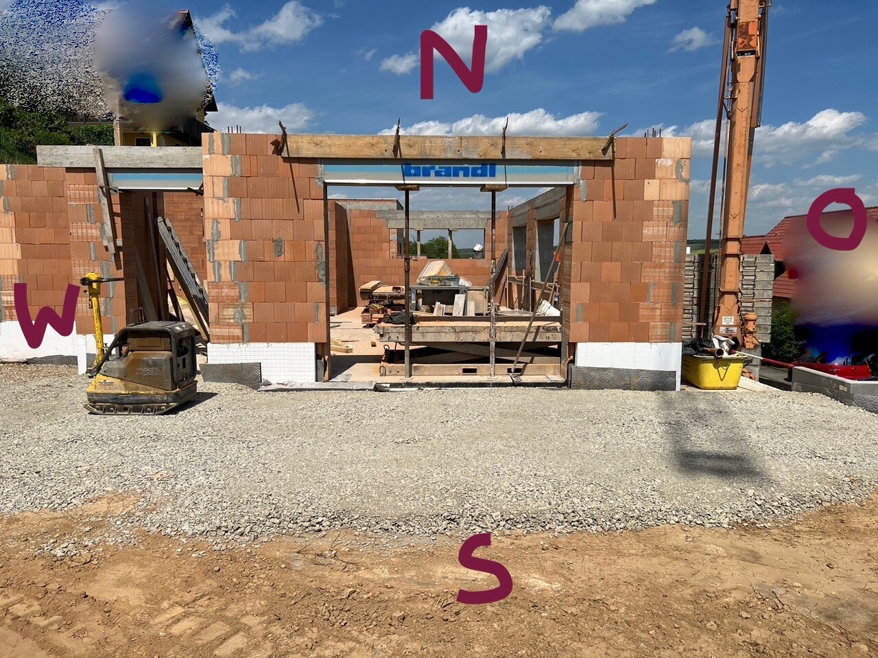 Baustelle mit rotem Ziegel-Rohbau, offenes Portal, Baugeräte links und rechts.