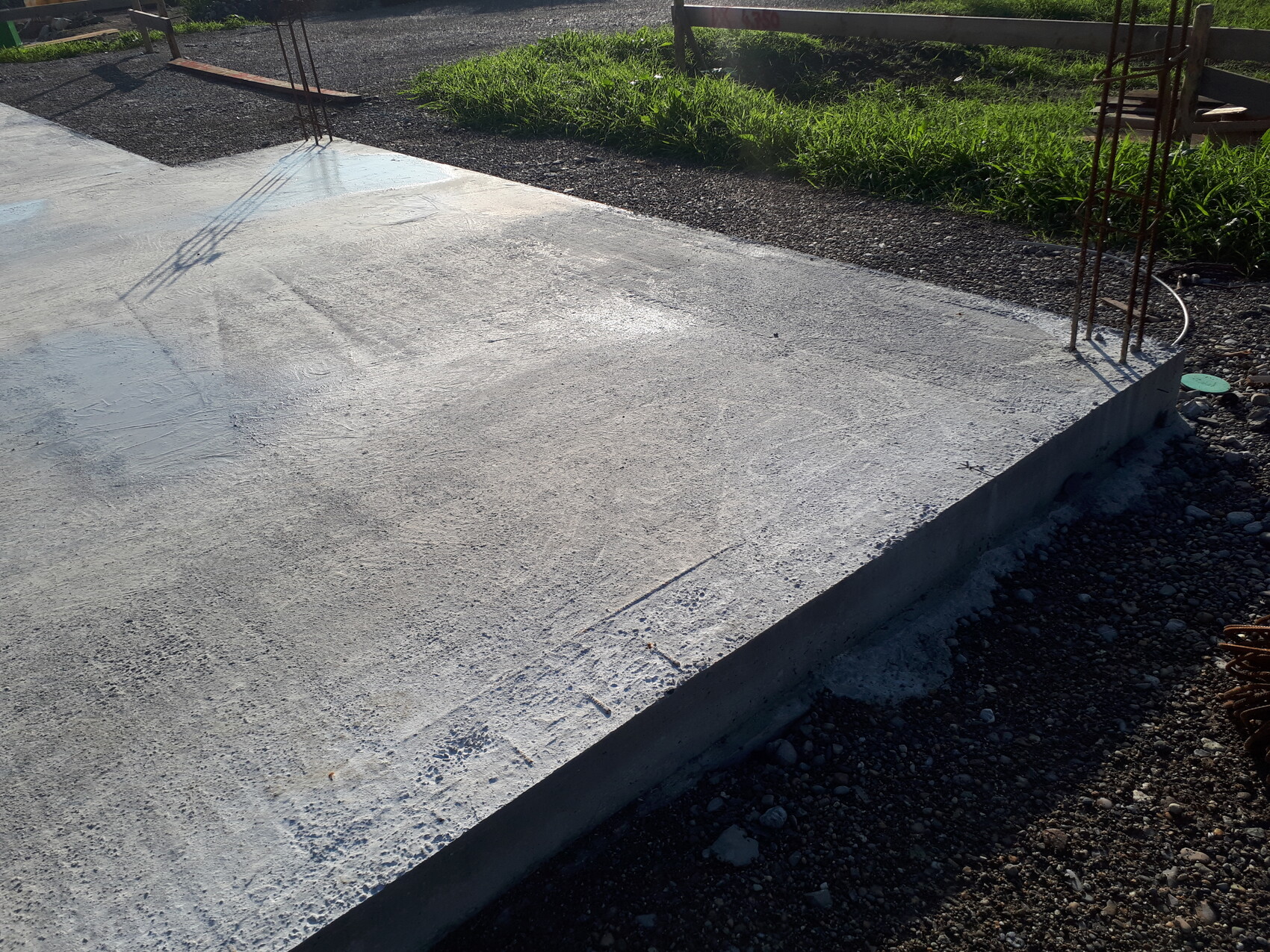 Frisch gegossene Betonplatte mit sichtbarer Bewehrung am Rand einer Baustelle