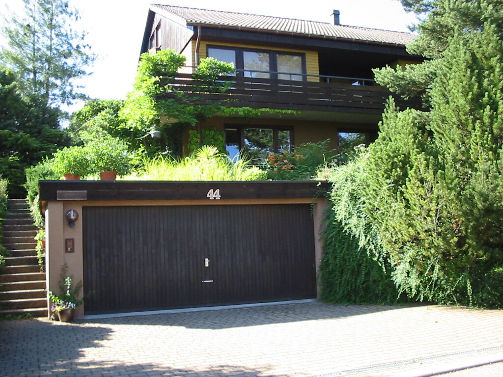 Zweistöckiges Haus mit dunkler Garage, 44, von Bäumen umgeben.