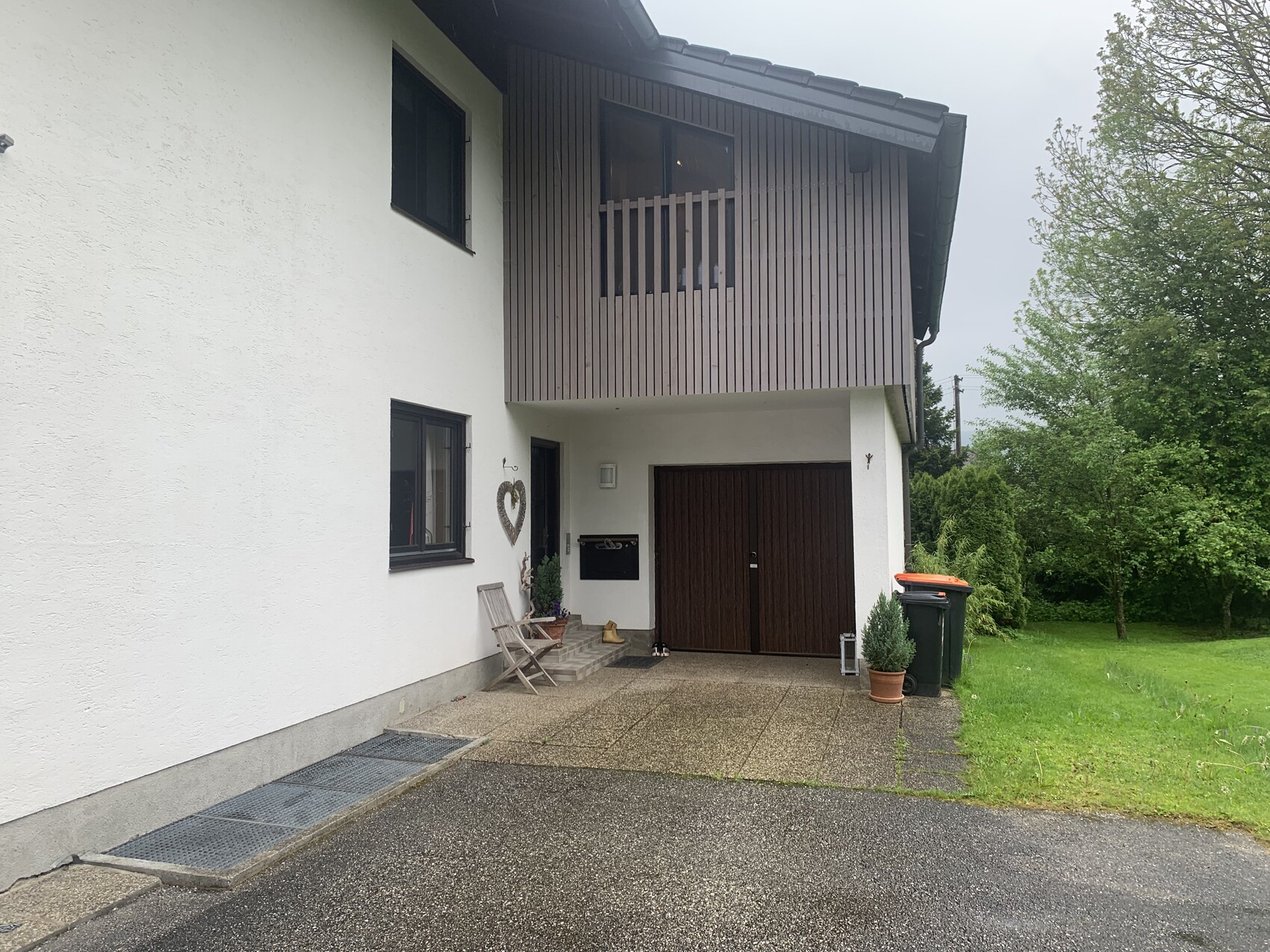 Außenansicht eines Hauses mit weißer Fassade, dunkler Holzverkleidung, Garage und Topfpflanzen.