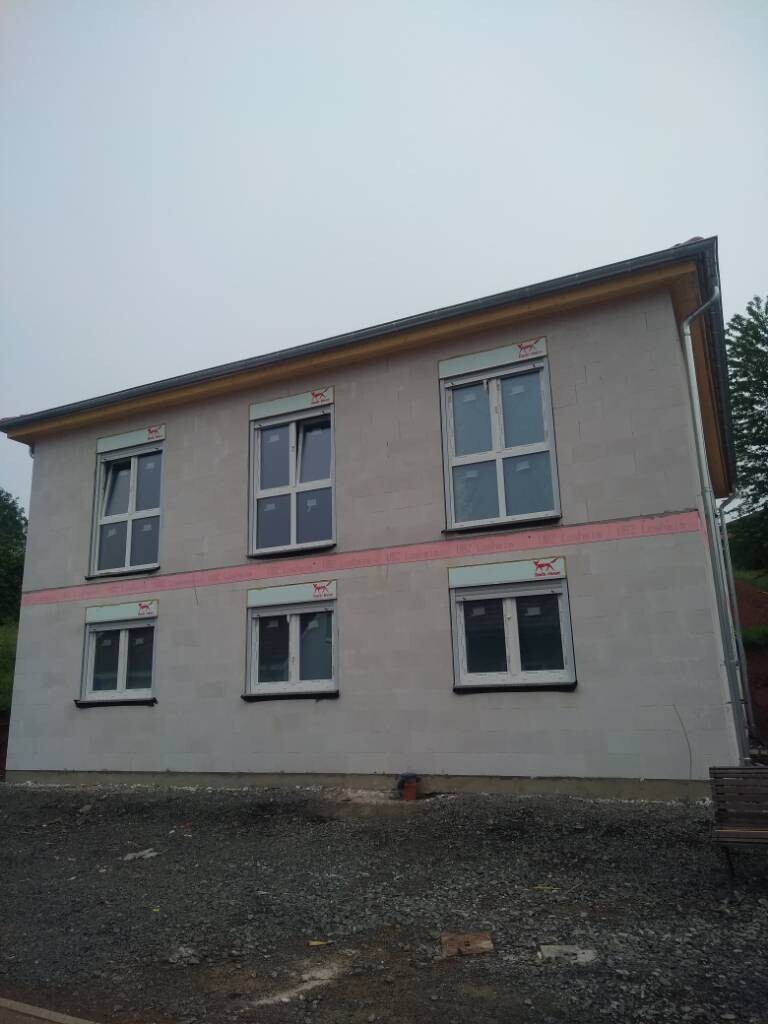 Zweistöckiges Haus im Bau mit Fenstern, rosa Fassadenband und Kiesboden davor