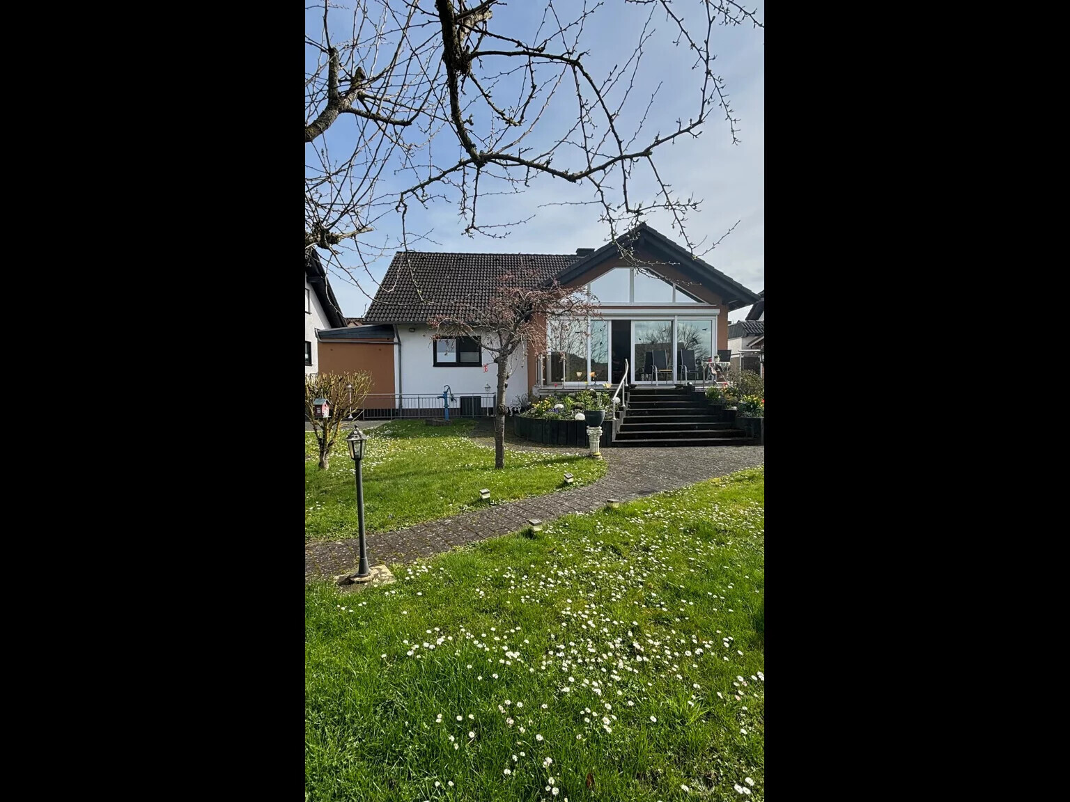 Einfamilienhaus mit Glasfront-Terrasse, Treppe und grünem Gartenweg im Vordergrund.