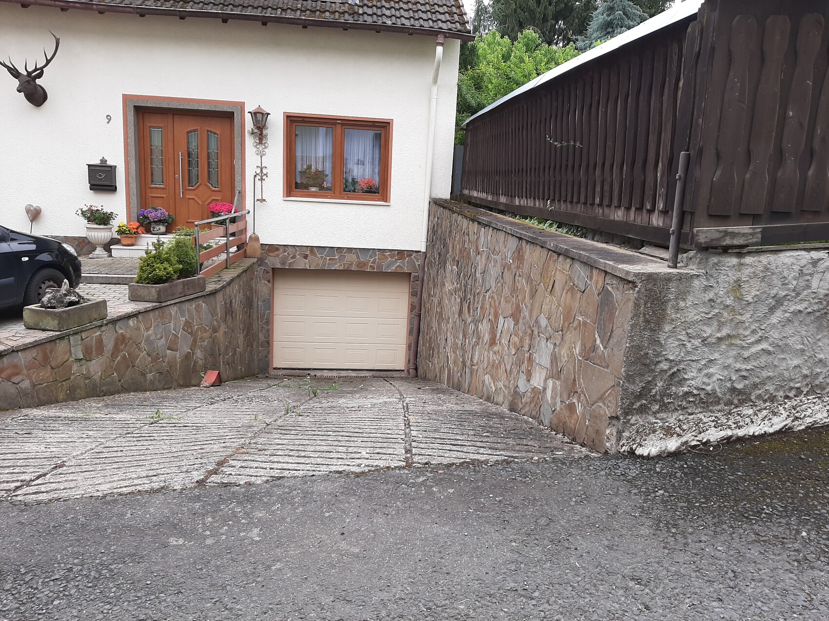Häuschen mit Holztür, Fenster und Blumenkästen; Rampe aus Stein führt zur Garage unter dem Haus.