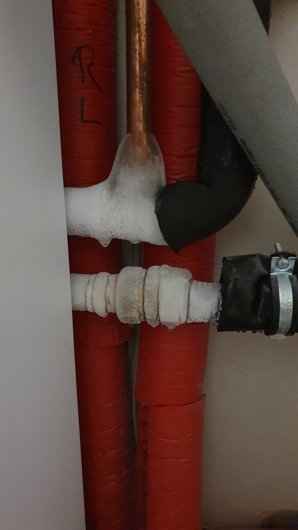 Rote Heizungsrohre mit Eisbildung an einer Verbindungsstelle und Armatur.