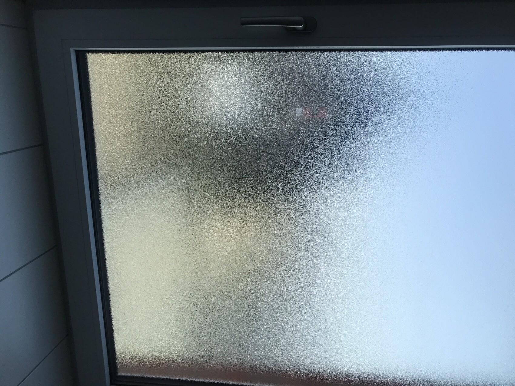 Milchiges Fenster mit Rahmen; unscharfe Silhouette hinter Glas, Griff oben.