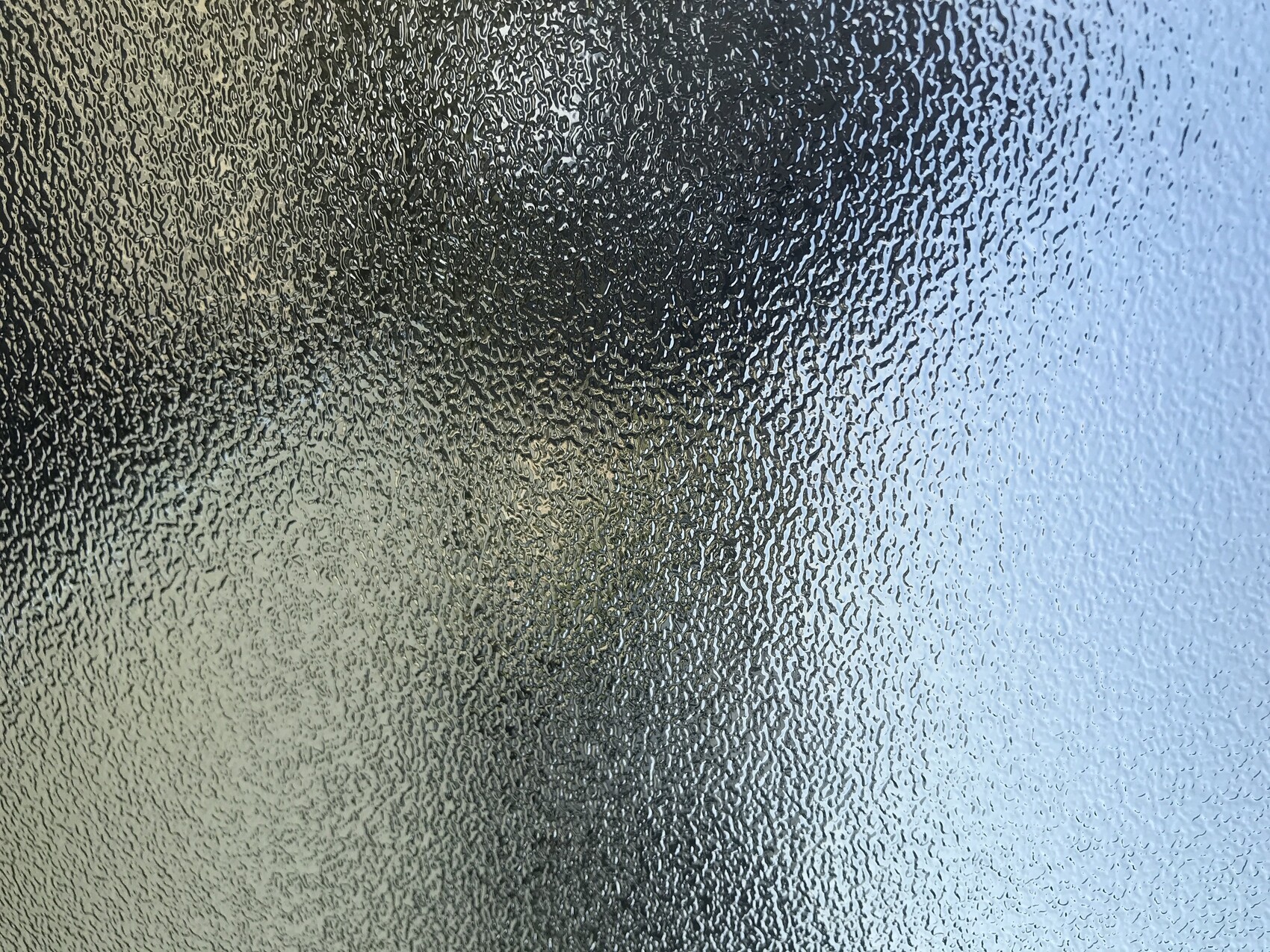Frostiges, strukturiertes Glasfenster; unregelmäßige Muster von links dunkel nach rechts hell.