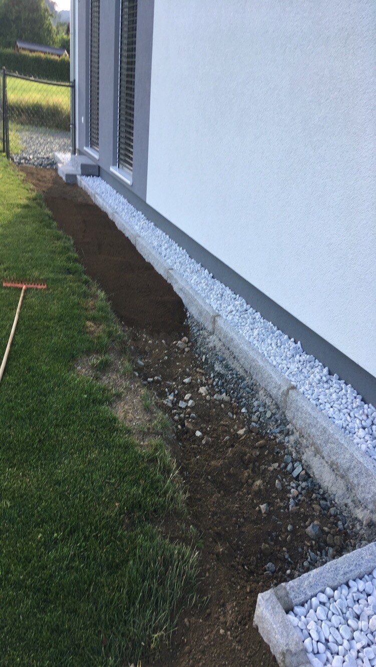 Außenwand eines Hauses; Fundamentstreifen mit Weißkies, Erdarbeiten neben dem Rasen