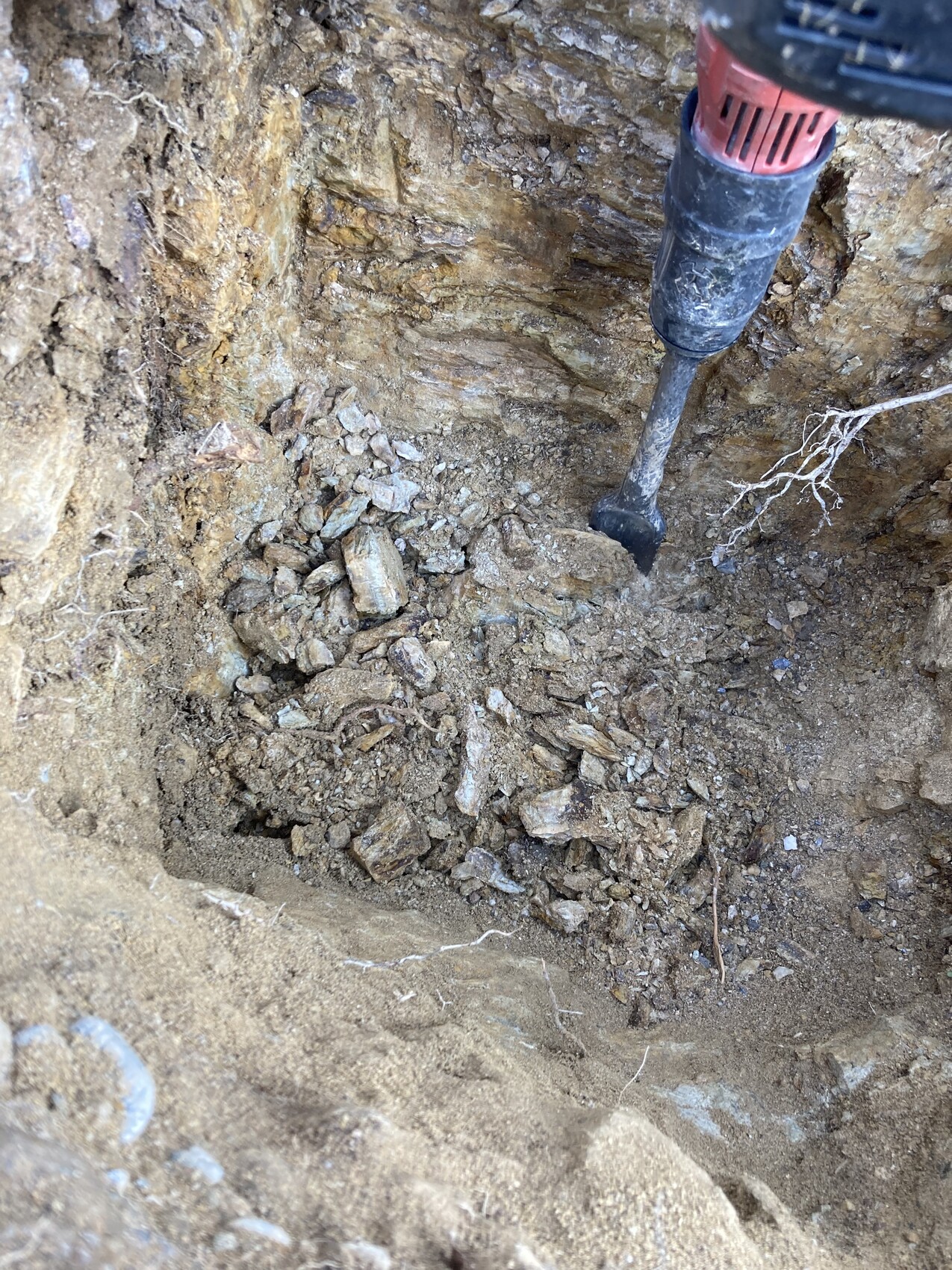 Bohrhammer im Erdloch mit losem Gestein, Steinen und Wurzeln beim Aushub.