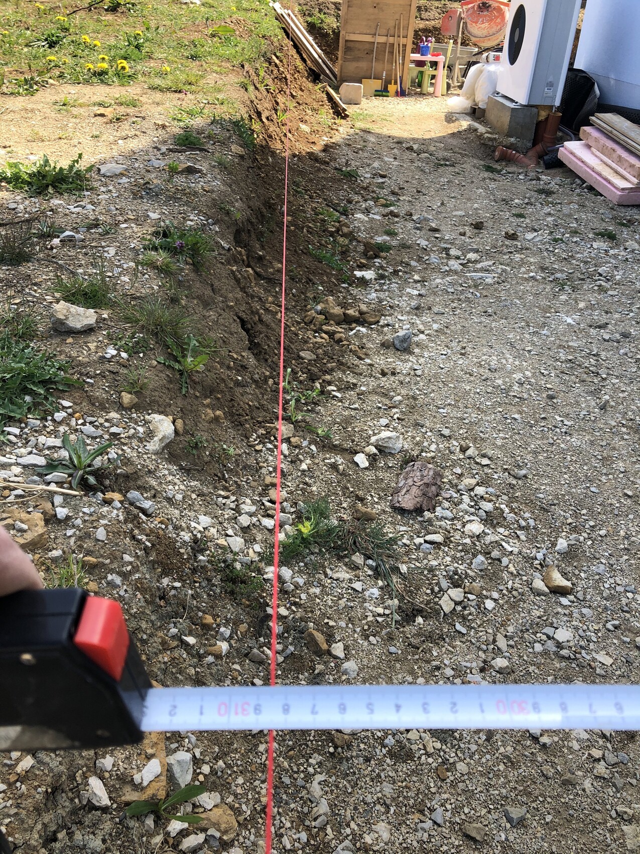 Baustelle mit tiefem Graben, rote Schnur als Vermessungslinie, Maßband im Vordergrund.