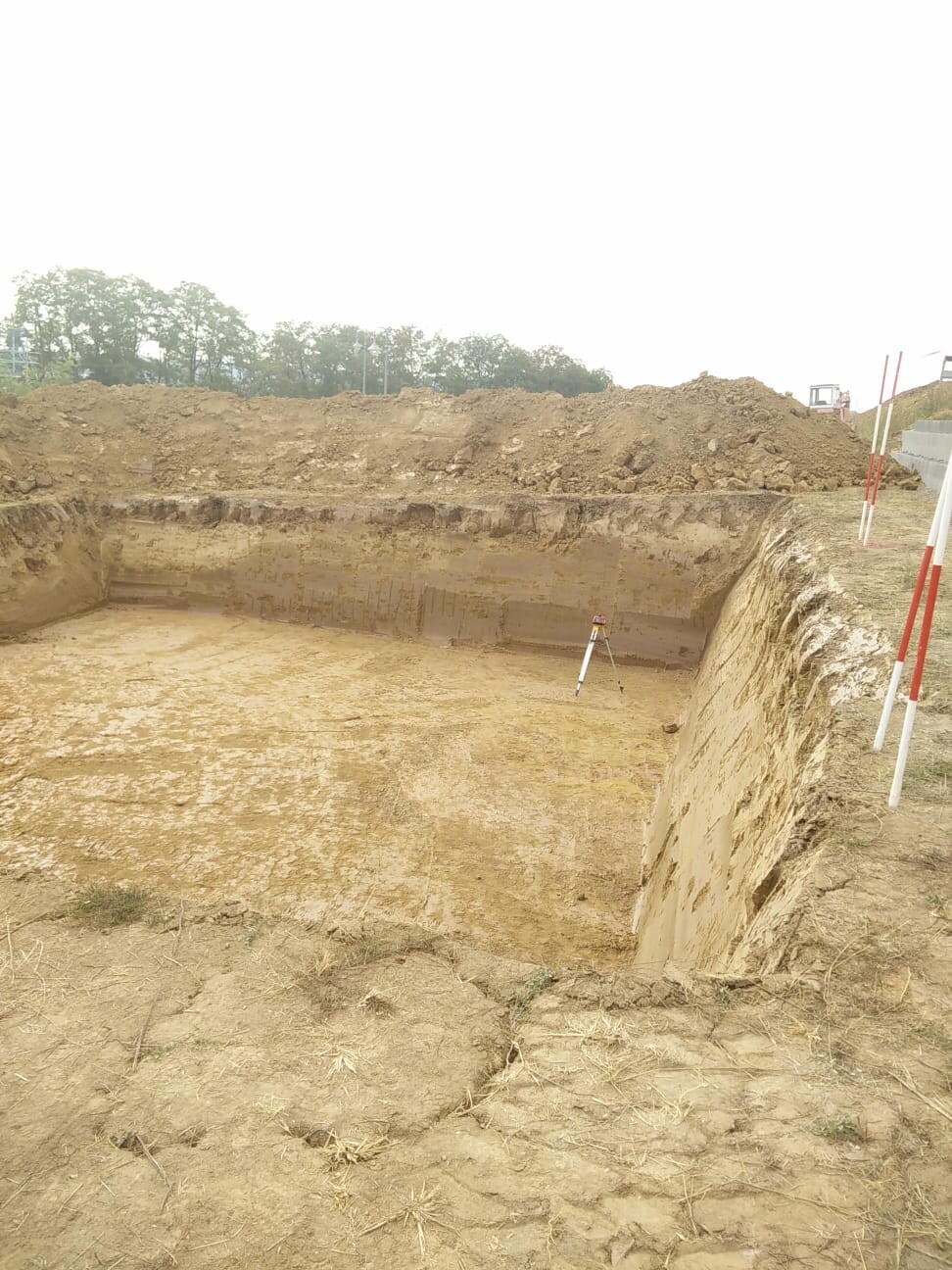 Große Baugrube mit Erdwand und Vermessungsgerät am Rand der Baustelle