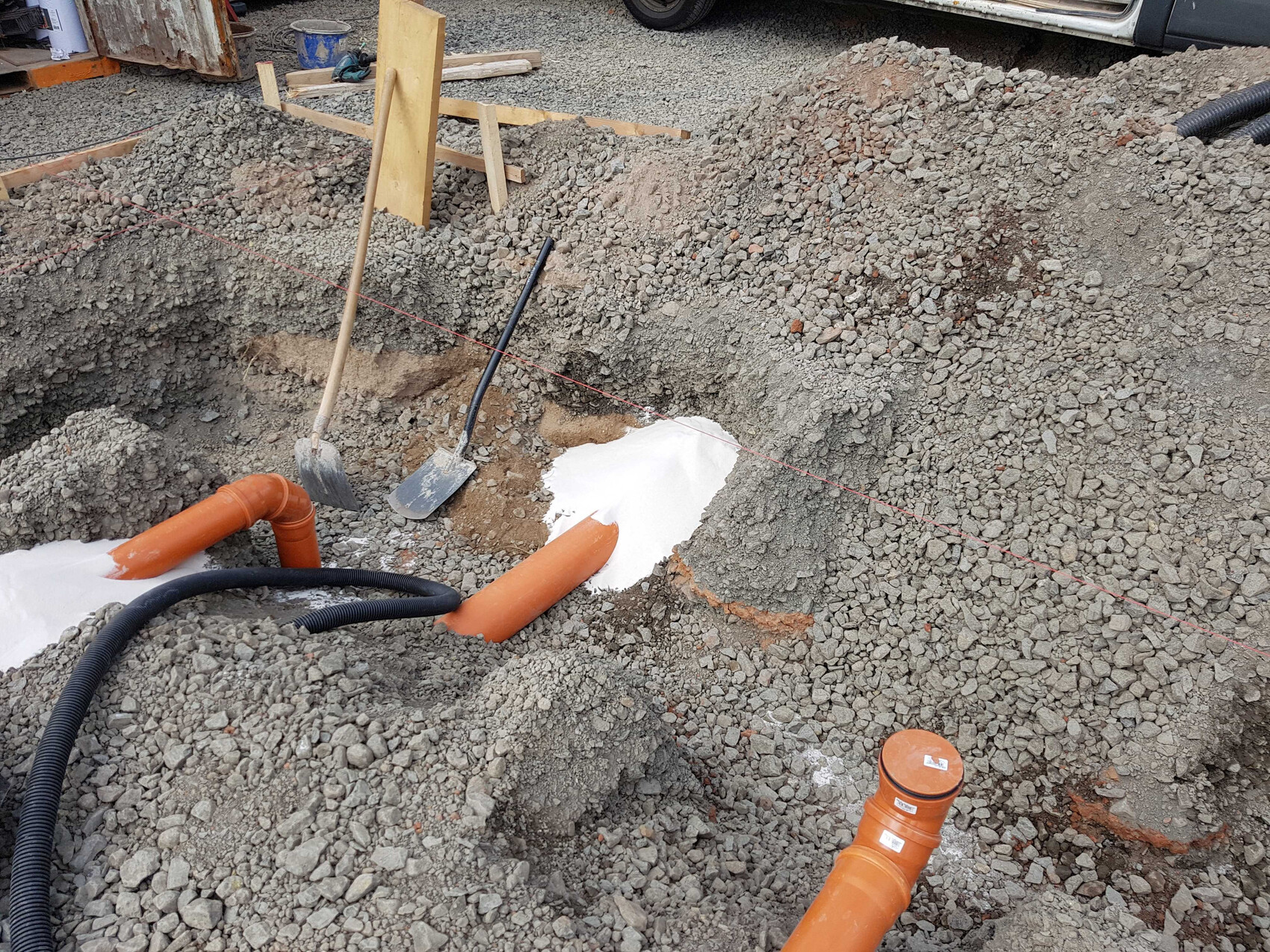 Grabungsbereich auf einer Baustelle mit orangefarbenen PVC-Rohren, Schaufeln, Spaten und roter Markierungslinie.