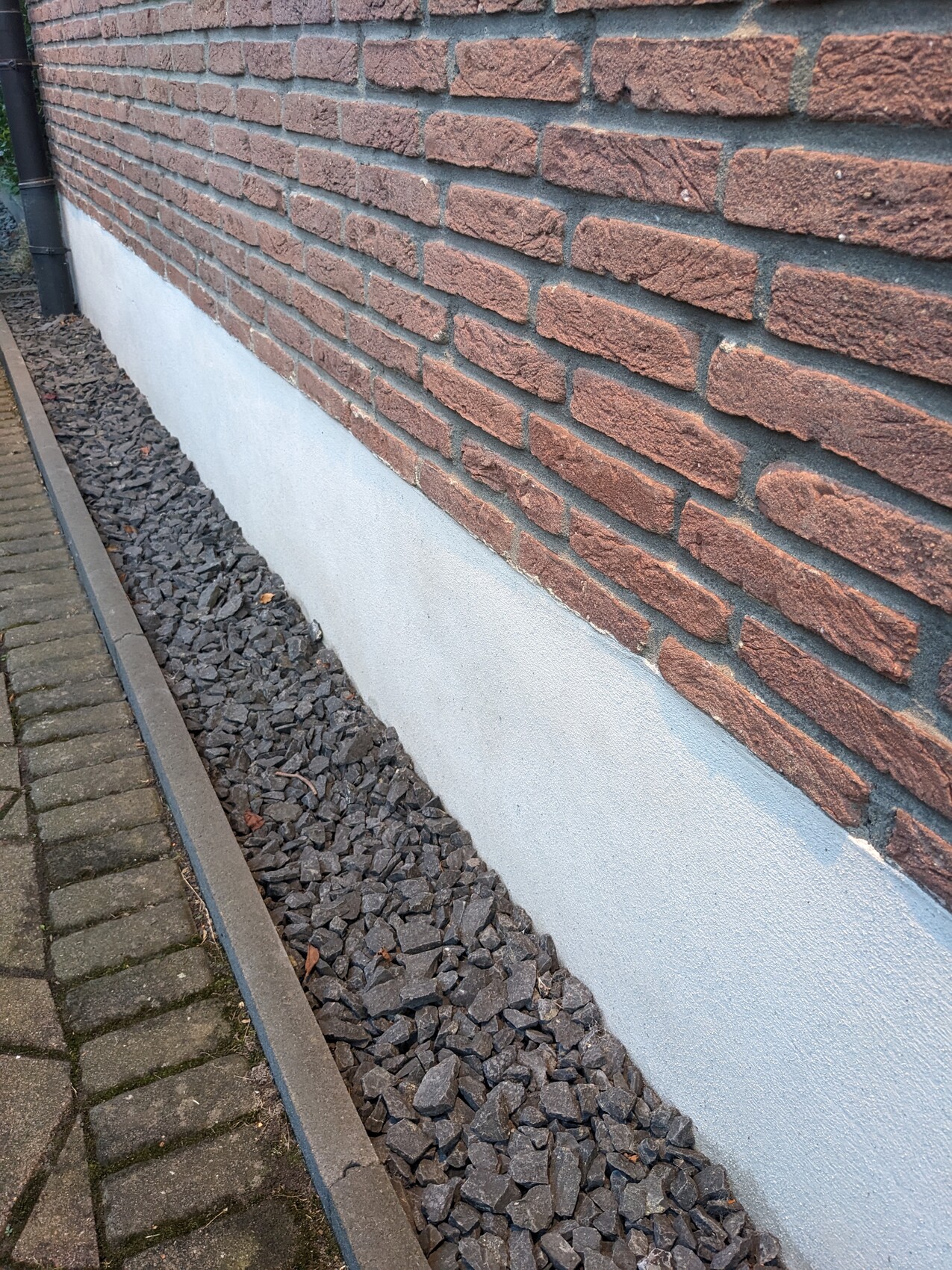 Außenwand aus roten Backsteinen über hellgrauer Betonfundament; Kieselsteinstreifen daneben.