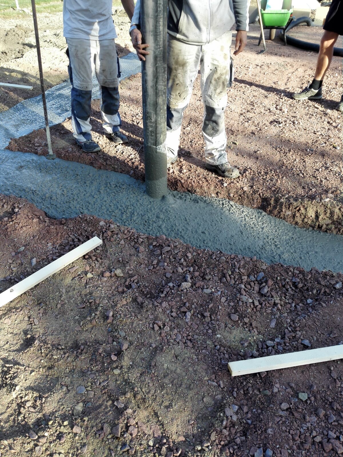 Bauarbeiter giessen Betonfundament in Graben auf Baustelle.