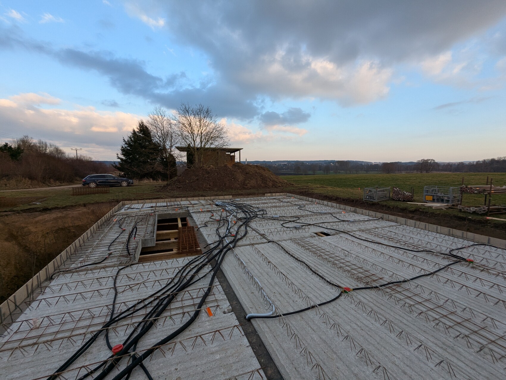 Fundamentplatte mit Bewehrung und Kabeln; Erdhaufen und ländliche Landschaft.