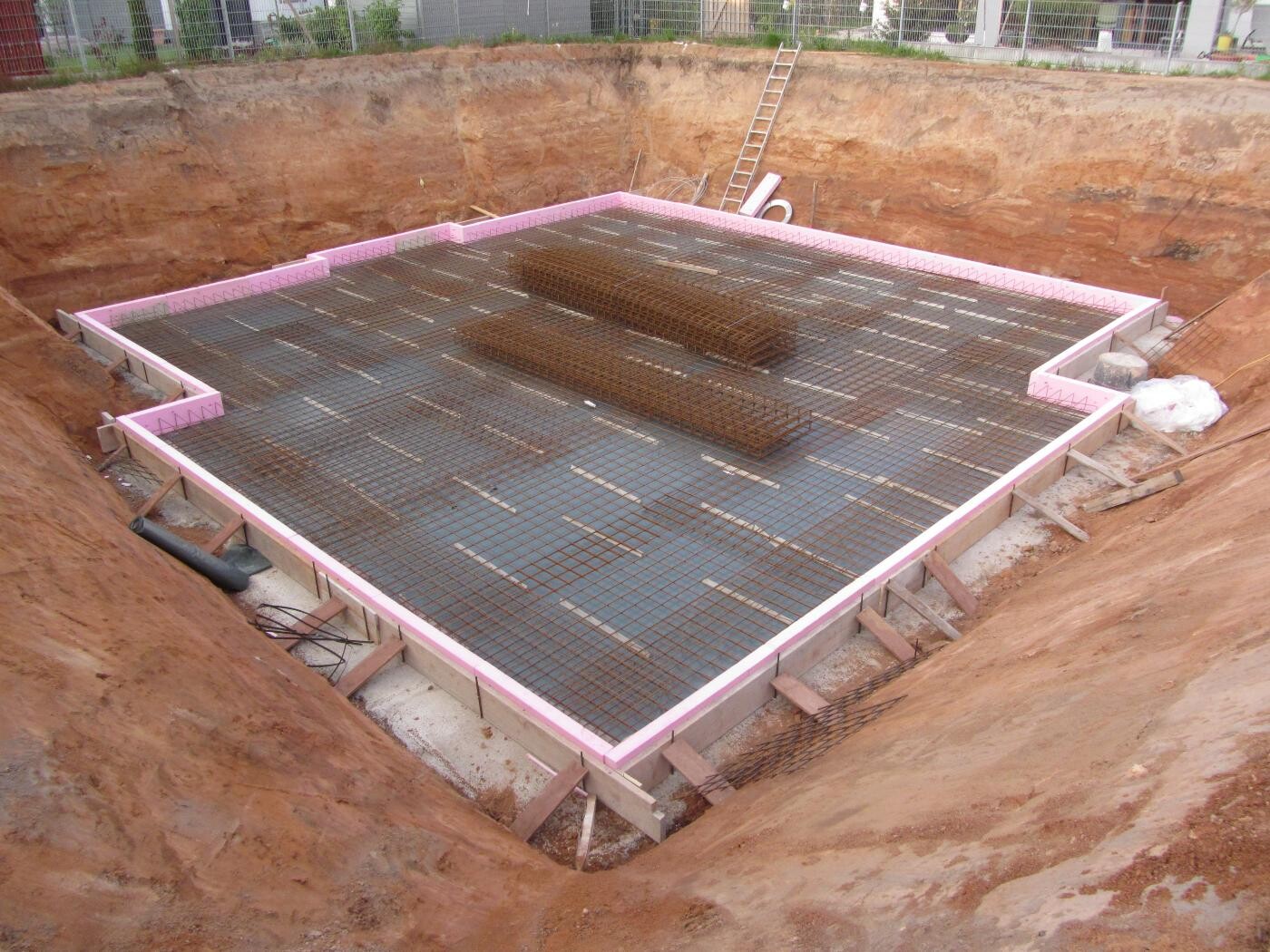 Baugrube für Fundament: Bewehrungsstahlgitter liegt bereit, Rand mit pinkem Dämmmaterial.