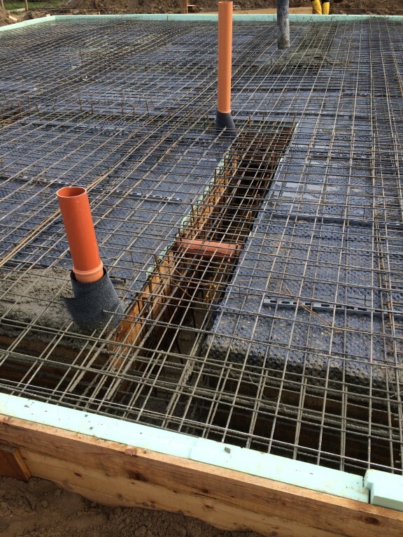 Fundamentplatte mit Bewehrung aus Stahlgitter, Holzform umrandet; orange Abflussrohre ragen hervor.