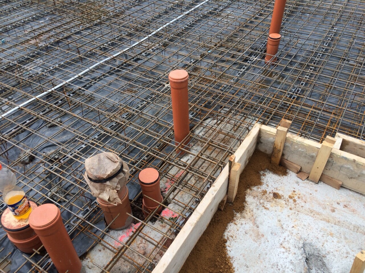 Baustelle mit Stahlbewehrung in Gittern, orange Rohre und Holzformen am Fundament