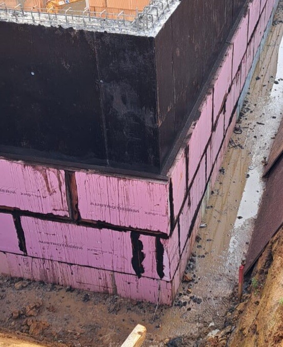 Fundamentbau mit pinken Styropor-Isolierblöcken, schwarze Oberabdichtung, Baugrube