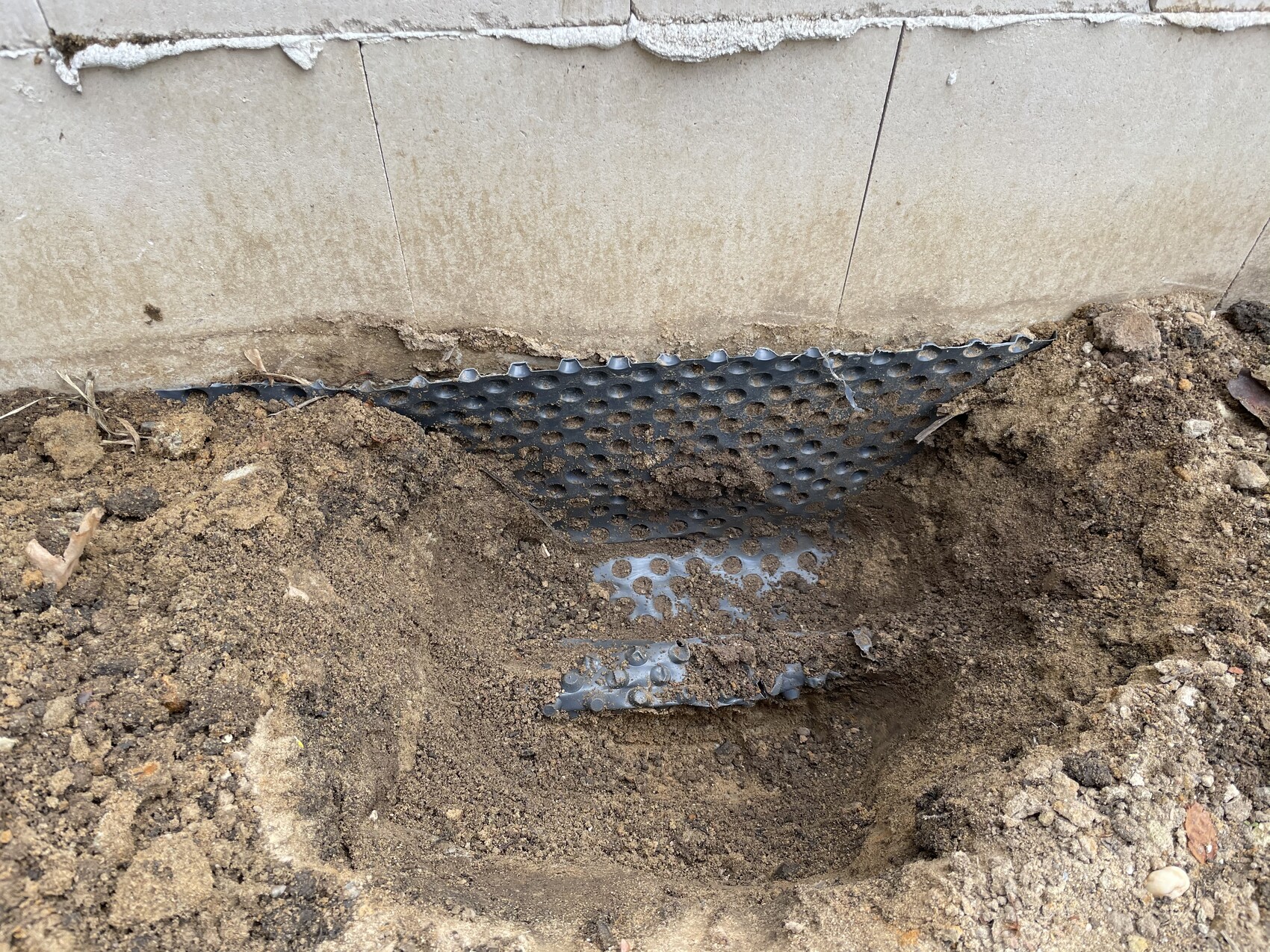 Graben neben dem Hausfundament; blaues perforiertes Drainage-Panel im Erdreich.