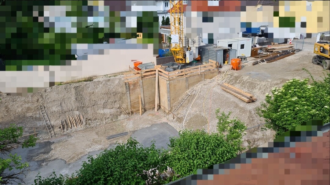 Baustelle mit Graben, Holzgerüst, Kran, Bauholz und Baumaschinen.