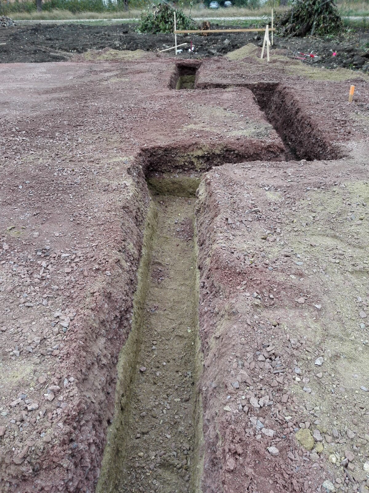 Ausgehobene Baugrube mit tiefen Gräben auf einer Baustelle und Erdreich an den Grabenrändern