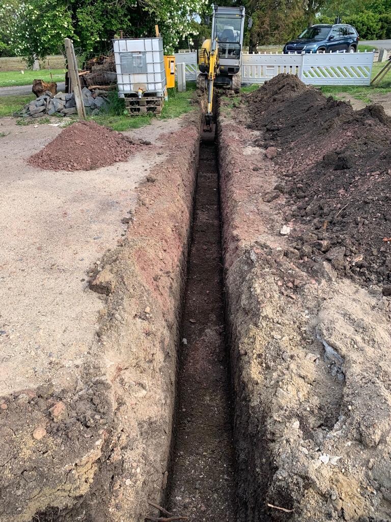 Bagger gräbt in einer Baugrube, seitlich liegen Erdberge; Baustelle mit Zäunen im Hintergrund.
