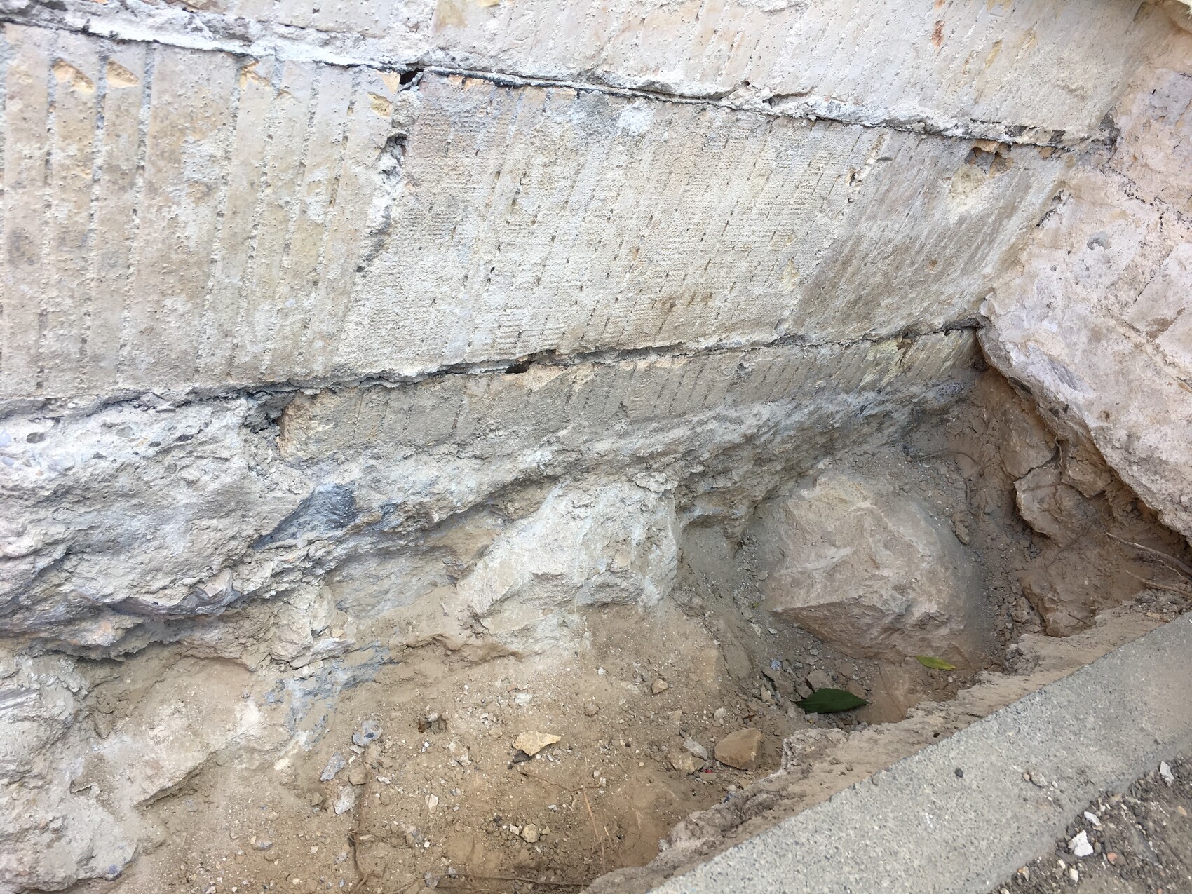 Baugrube neben Fundamentmauer mit Erde und Steinen sichtbar