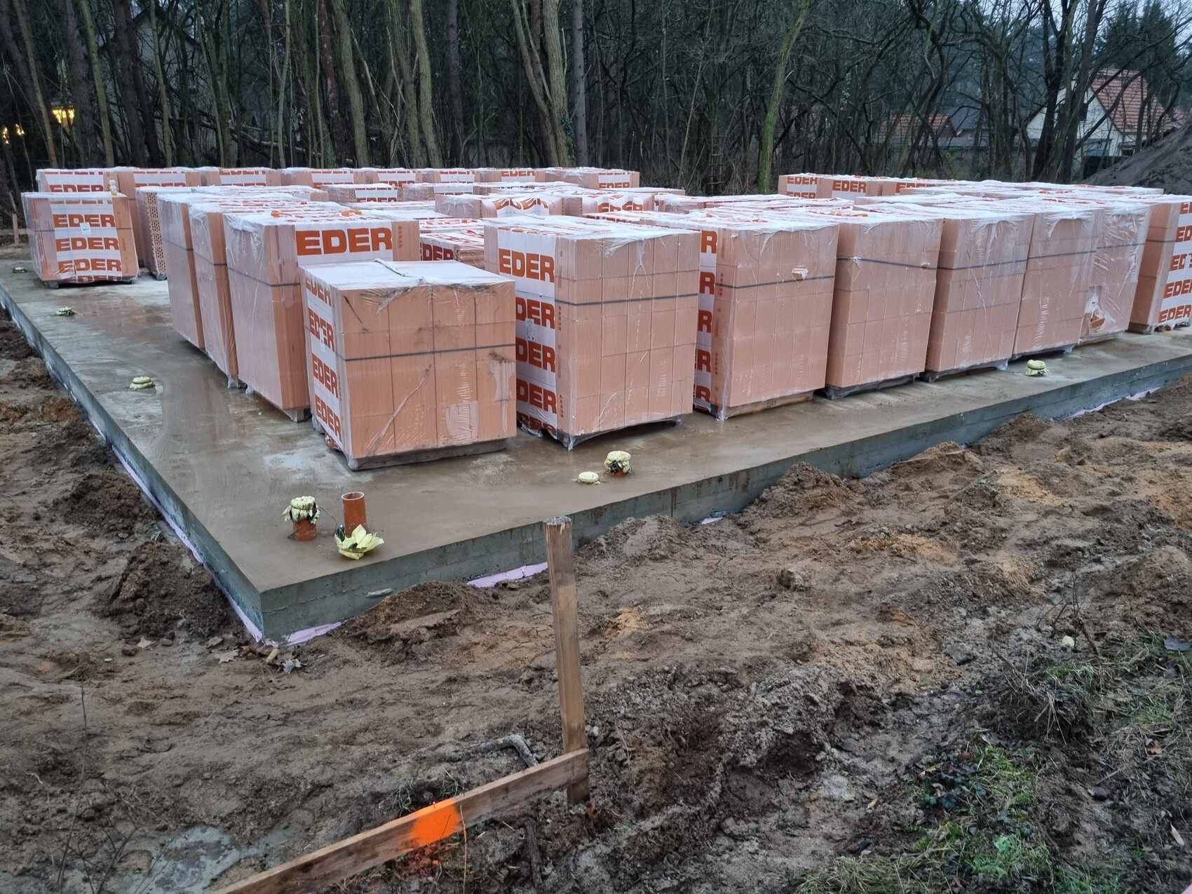 Baustelle: auf Betonplatte stapelbare Baumaterial-Pakete mit EDER-Aufdruck, umgeben von Erde.