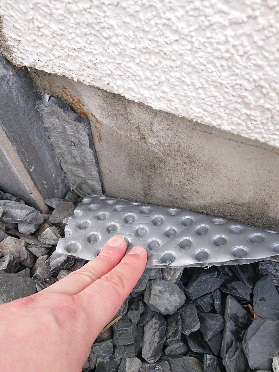 Nahaufnahme: Finger tippt auf silberne Metallplatte mit runden Mulden am Fundament, Kies.