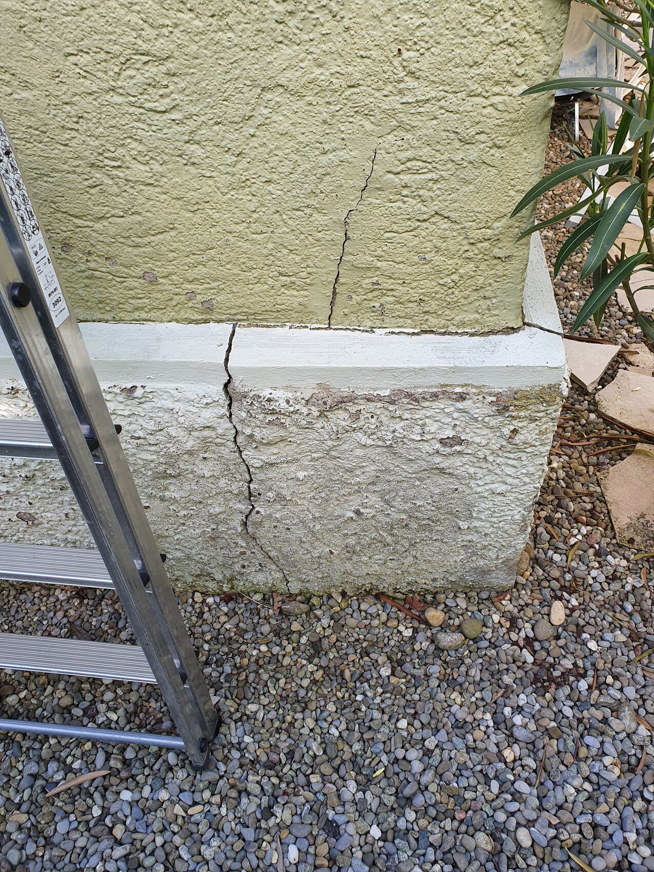 Außenwand-Fundament mit grobem Riss; Leiter davor, Kiesboden.